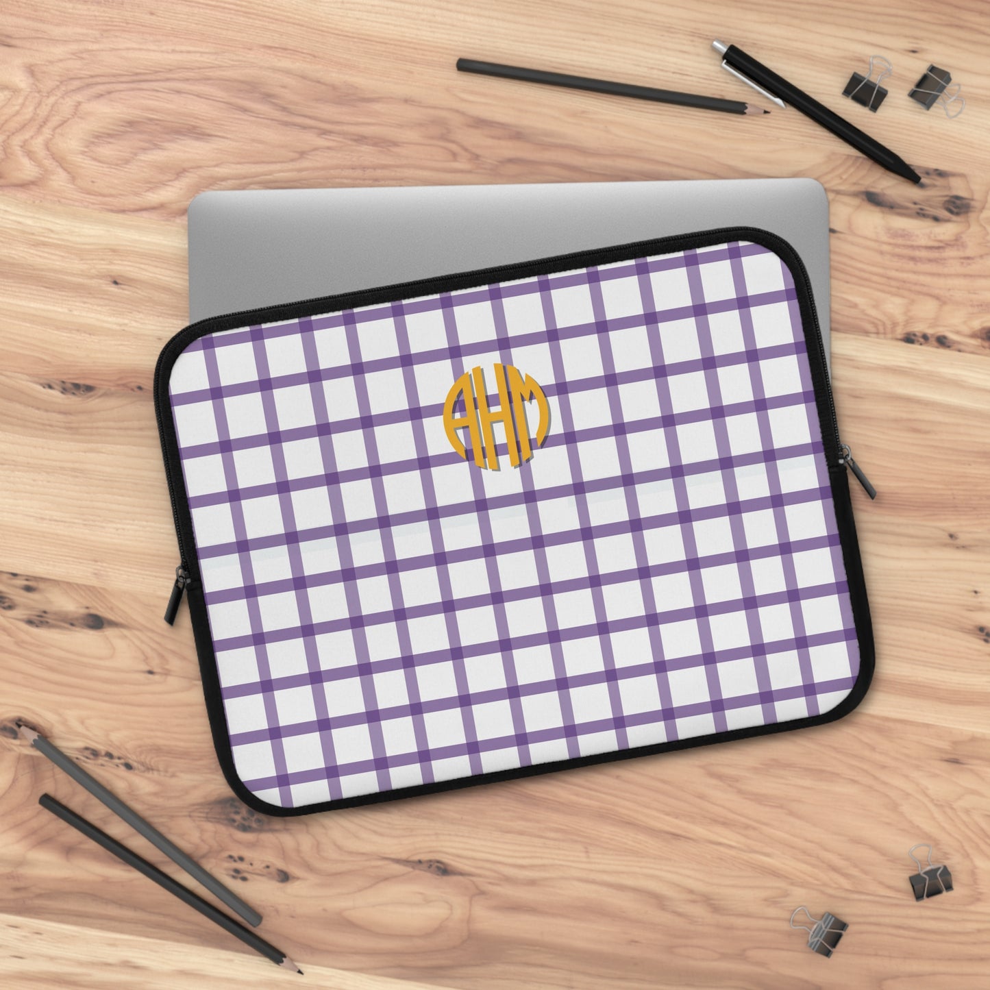 Purple and white checkered laptop sleeve with a yellow monogram on a wooden surface.