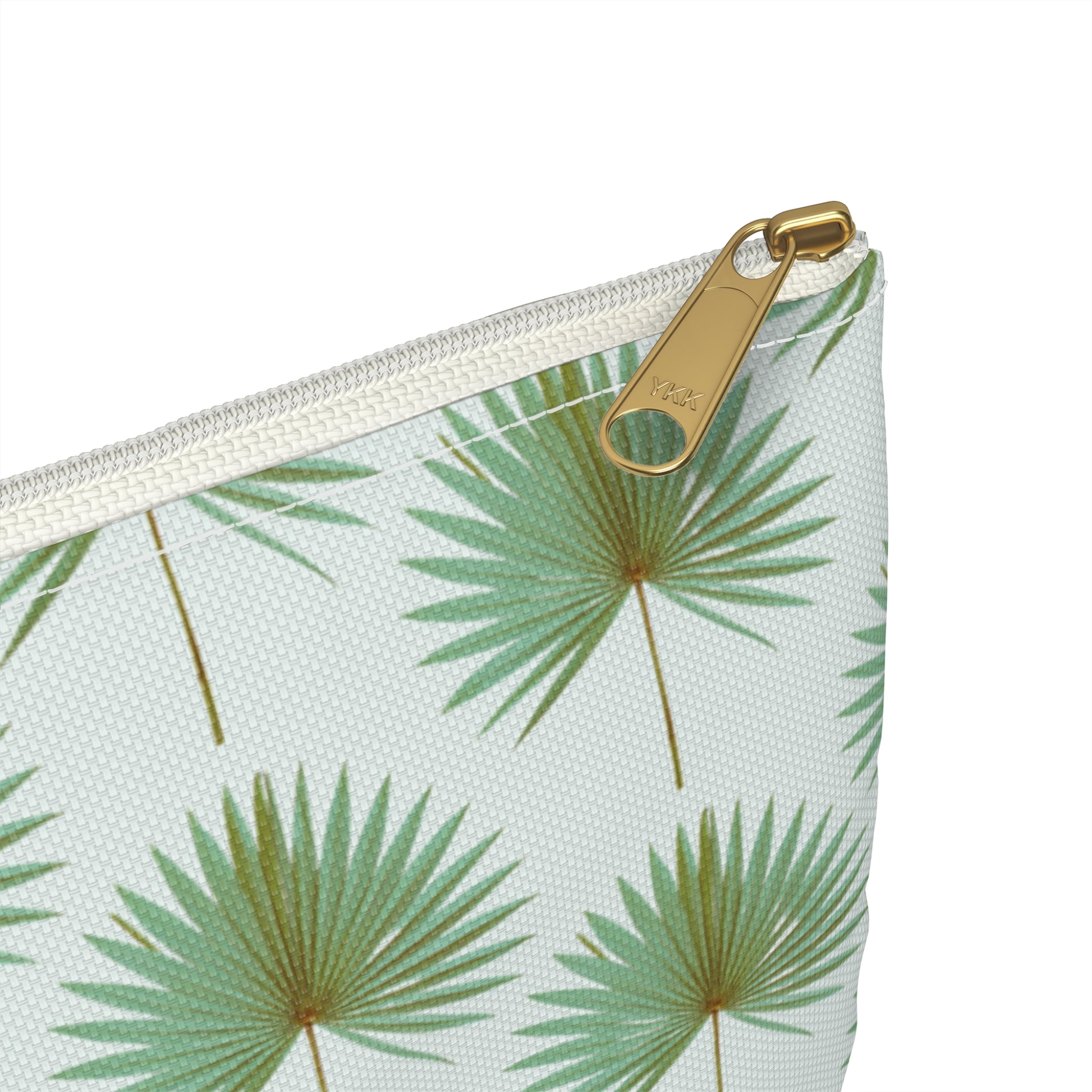 close up view of zipper of cosmetic travel bag with repeating pattern of green fan palm leaves on white backgroun