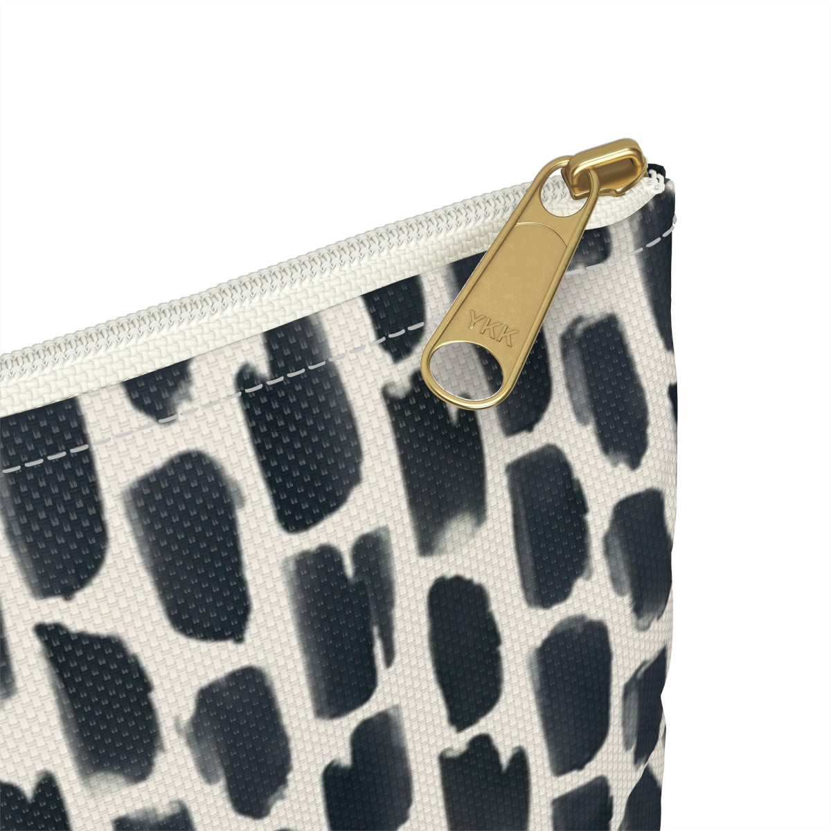 Close up view of gold zipper on personalized cosmetic travel bag with white monogram letters on a background of repeating abstract black and cream animal print design