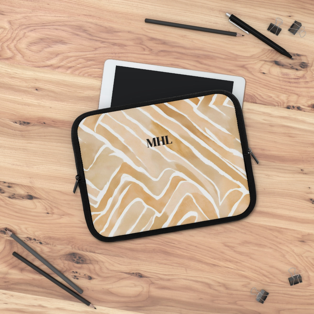 Monogrammed neoprene laptop case in a light tan, apricot  and cream abstract pattern on a desk