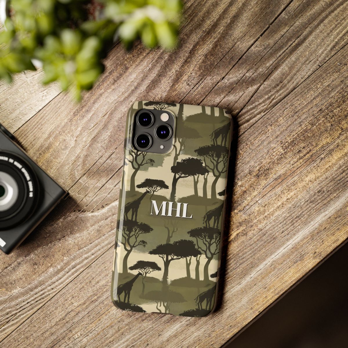 Front view of personalized slim iPhone case with white monogram on background of repeating giraffe and tree silhouettes in olive green, cream and black.